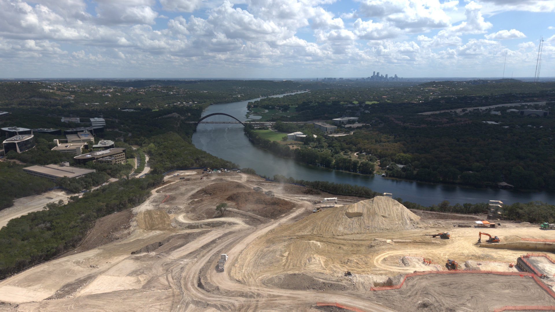 Aerial view of Lake Austin and wooded Hill Country, with Pennybacker Bridge, downtown Austin in the distance and construction in the foreground.