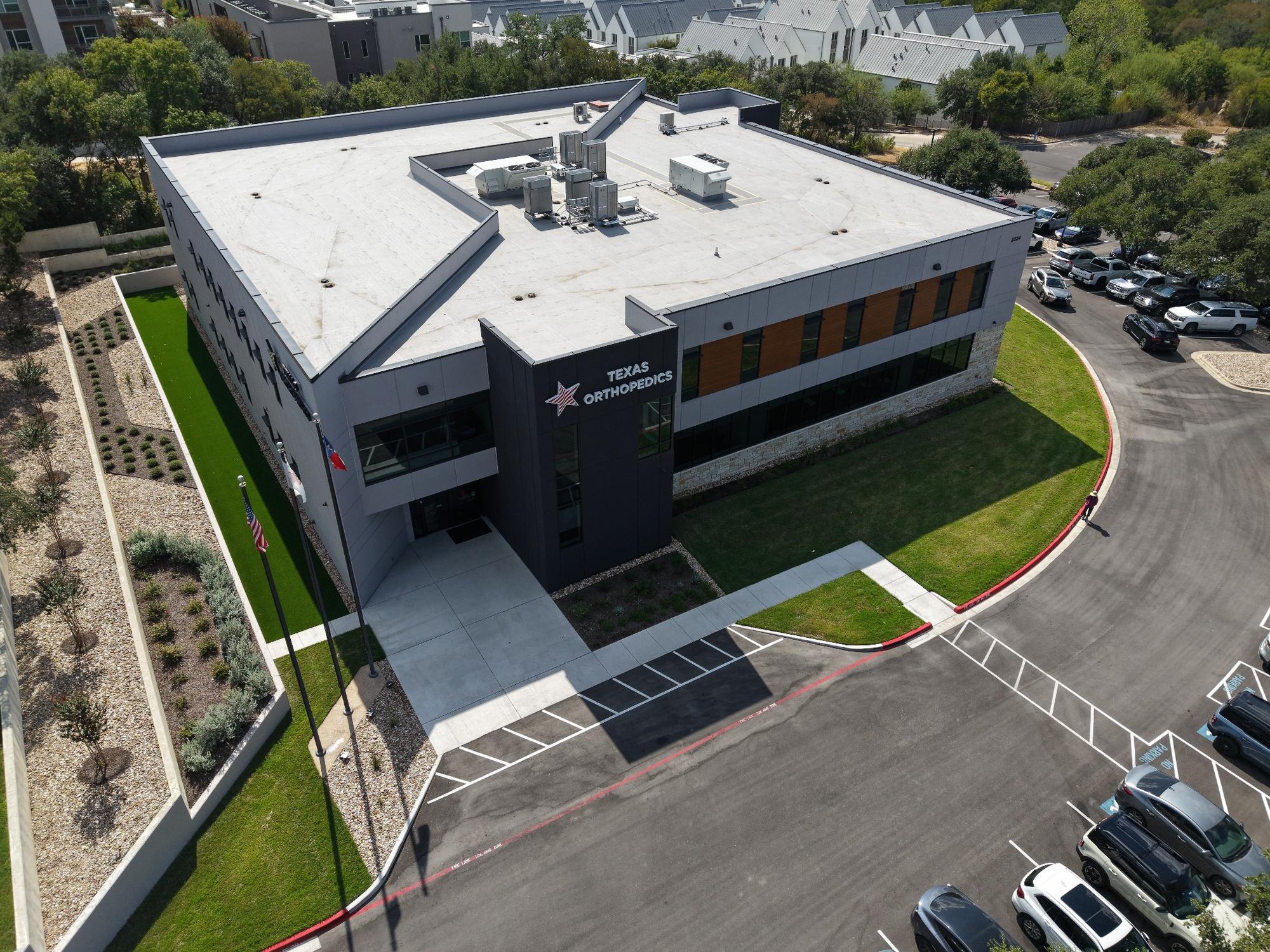 Aerial view of the Texas Orthopedics building in Austin, Texas, showing its entrance, rooftop, and surrounding parking.